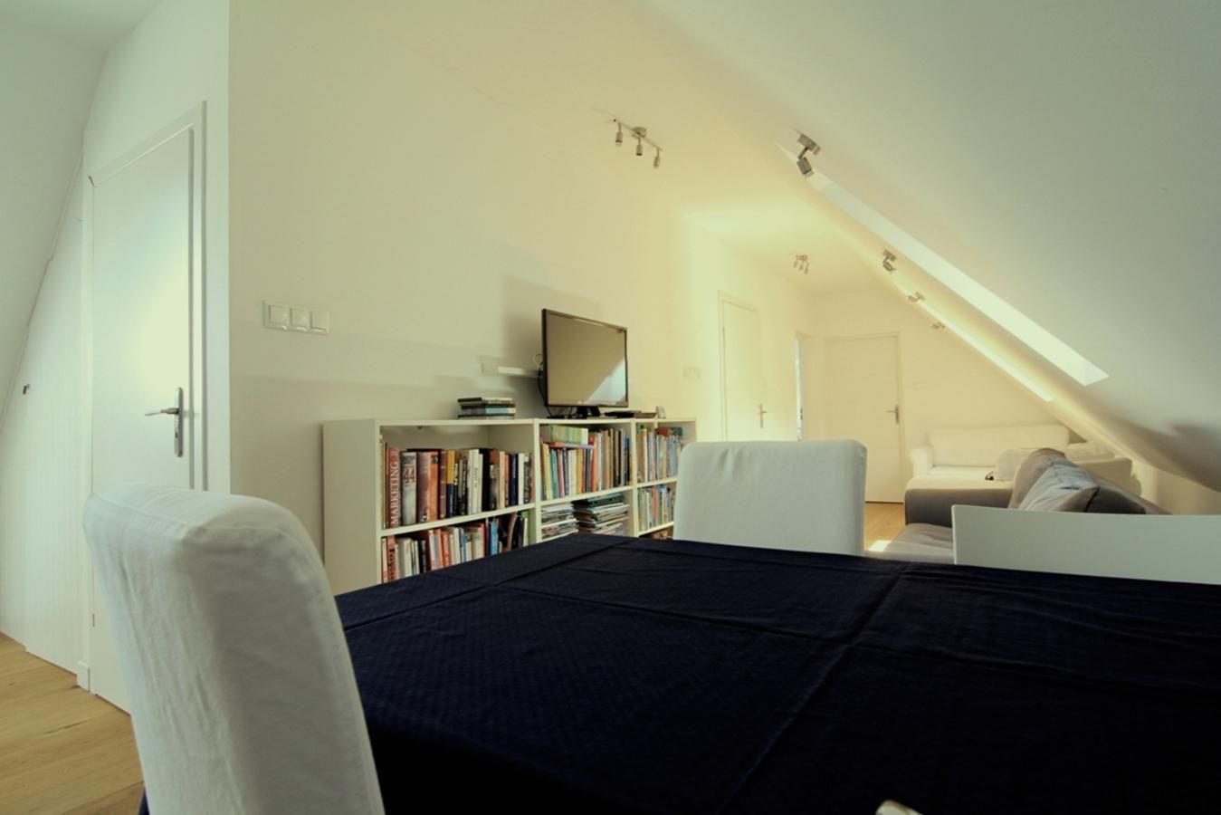 Et soveværelse med en seng, en hvid stol, en bogreol, et fjernsyn og en sofa.
