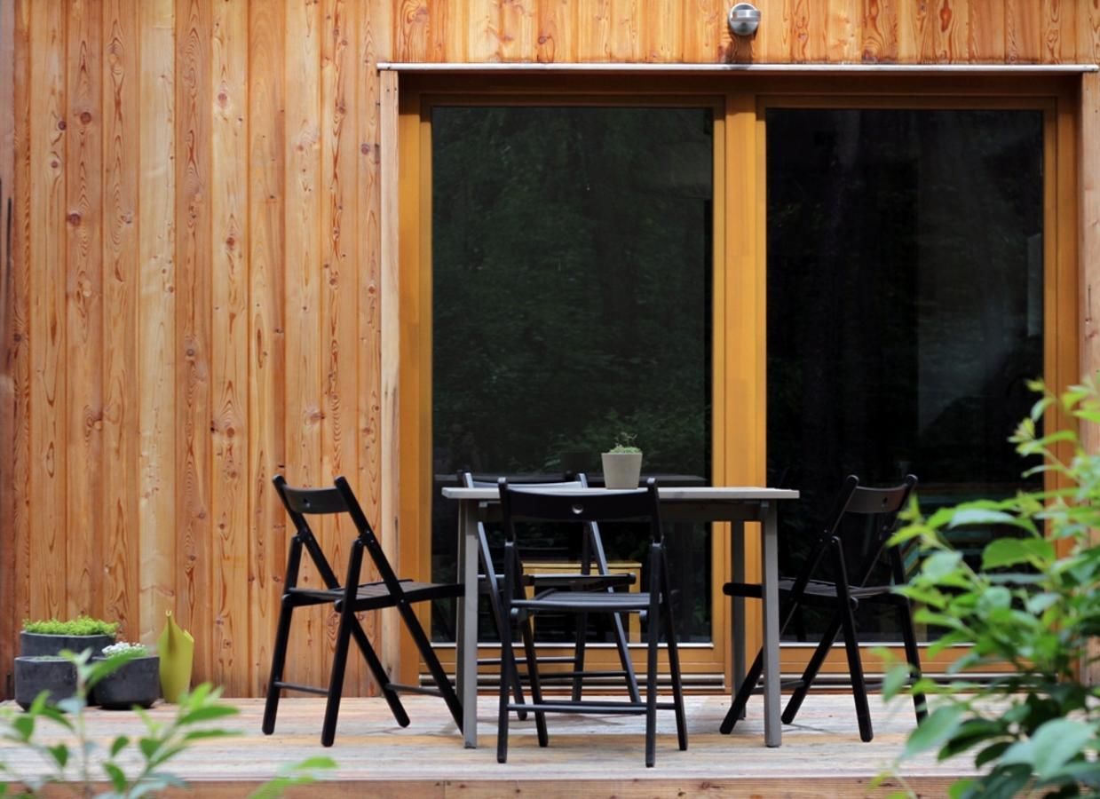 A wooden exterior wall with a sliding glass door leading to a patio area with a table and chairs.