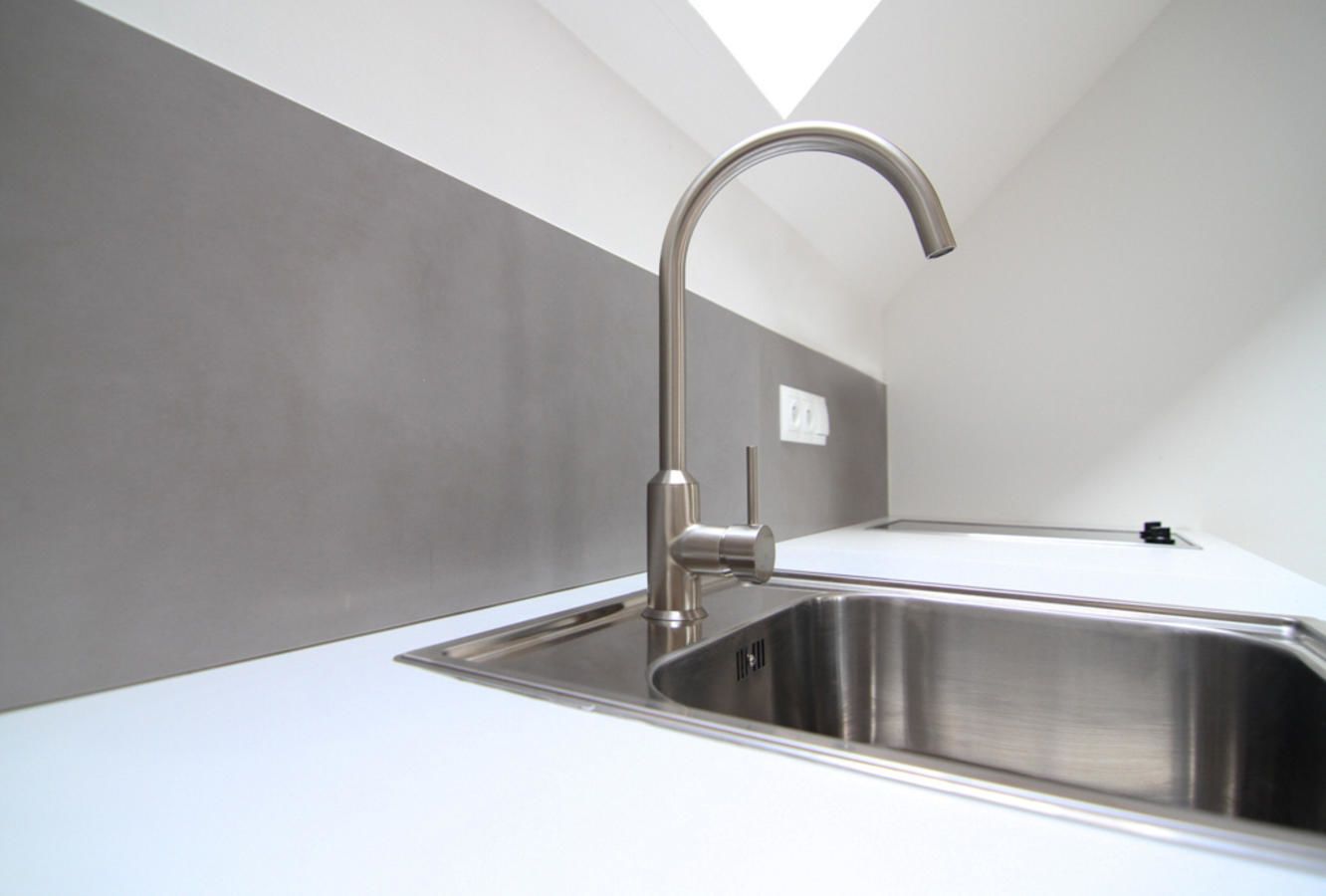 A modern kitchen with a stainless steel sink and faucet, a white countertop, and a grey wall.