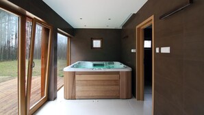 Um banheiro moderno com hidromassagem, janelas amplas e vista para uma floresta.