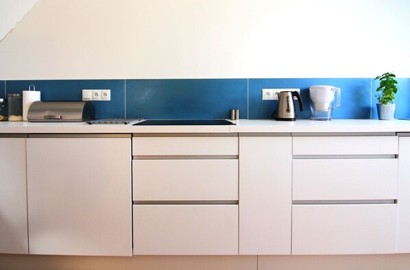 A modern kitchen with white cabinets, a blue backsplash, and various appliances including a coffee maker and a kettle. - Osada Osjaków (Osjakow)