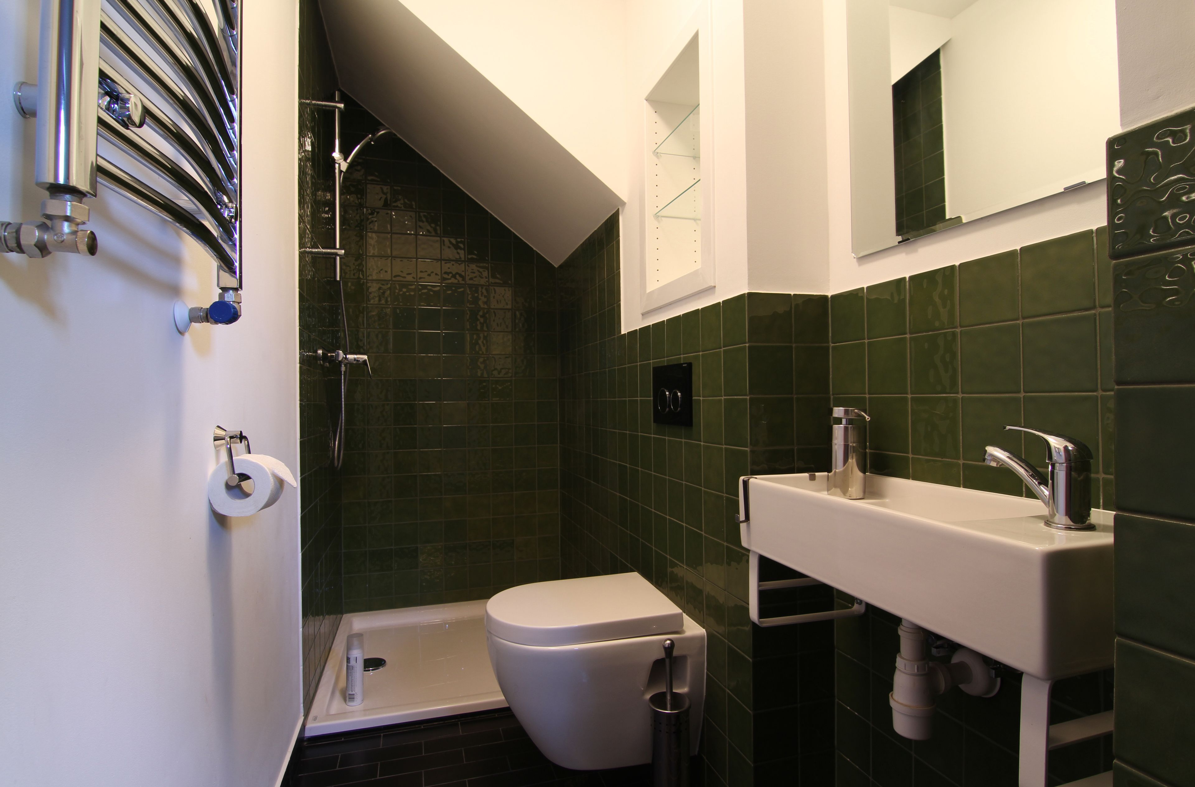 Un baño con inodoro blanco, ducha y lavamanos con espejo.