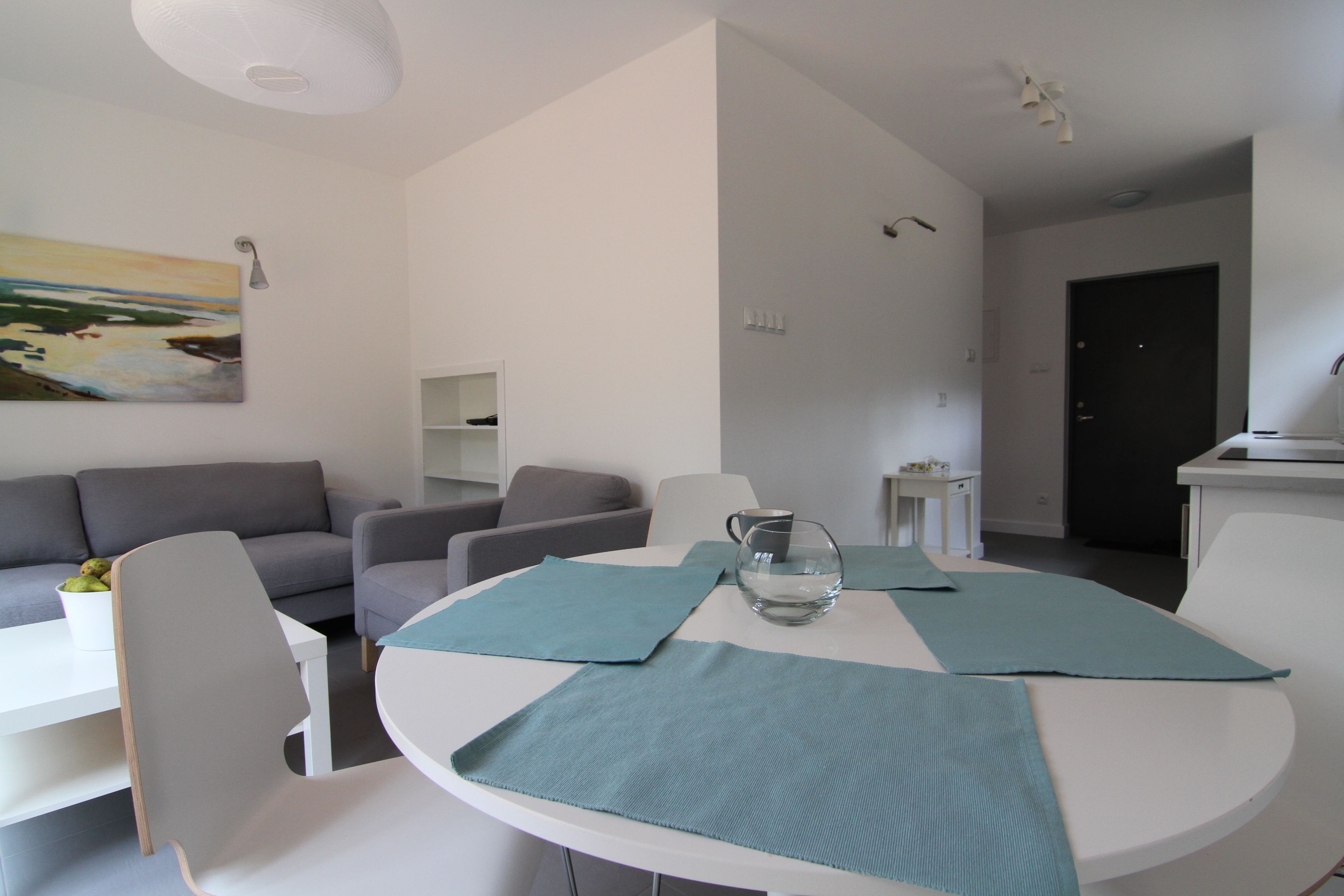 A modern living room with a white table, teal placemats, and a grey sofa.