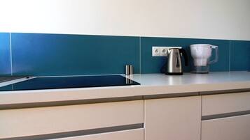 Una cocina con una placa de inducción negra, un hervidor de acero inoxidable y una cafetera sobre la encimera.