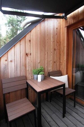 A wooden deck with a table and two chairs, a potted plant, and a glass door leading to an interior space. - Osada Osjaków (Osjakow)