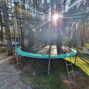 A trampoline in a forested area with a safety net and a ladder. - Osada Osjaków (Osjakow)