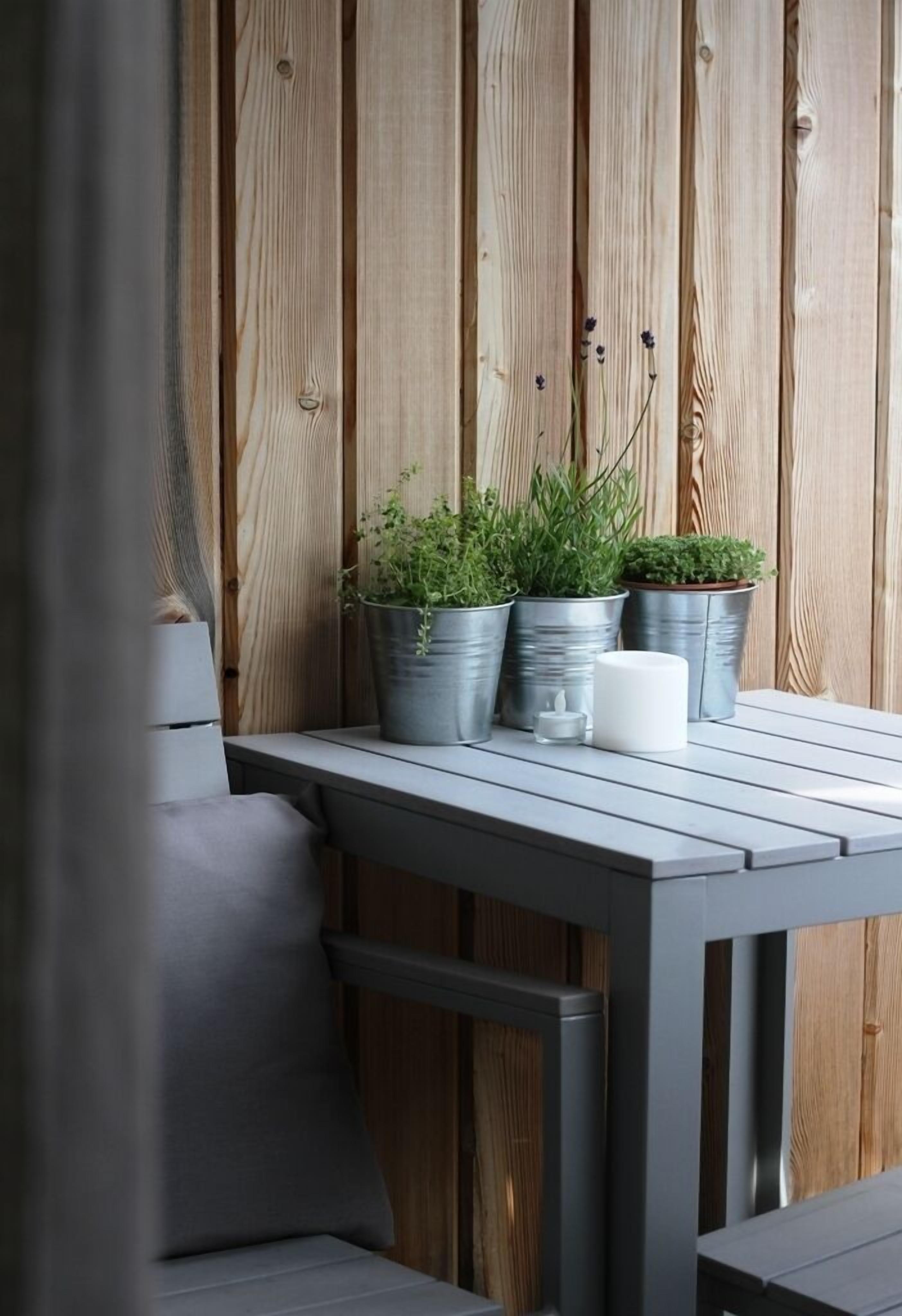 Parede de madeira com ripas verticais, uma mesa de metal com plantas em vasos e uma vela branca.