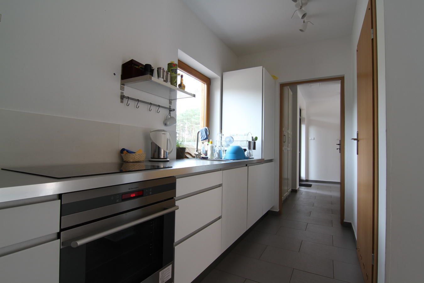 Una cocina moderna con armarios blancos, electrodomésticos de acero inoxidable y un ventanal que proporciona luz natural.