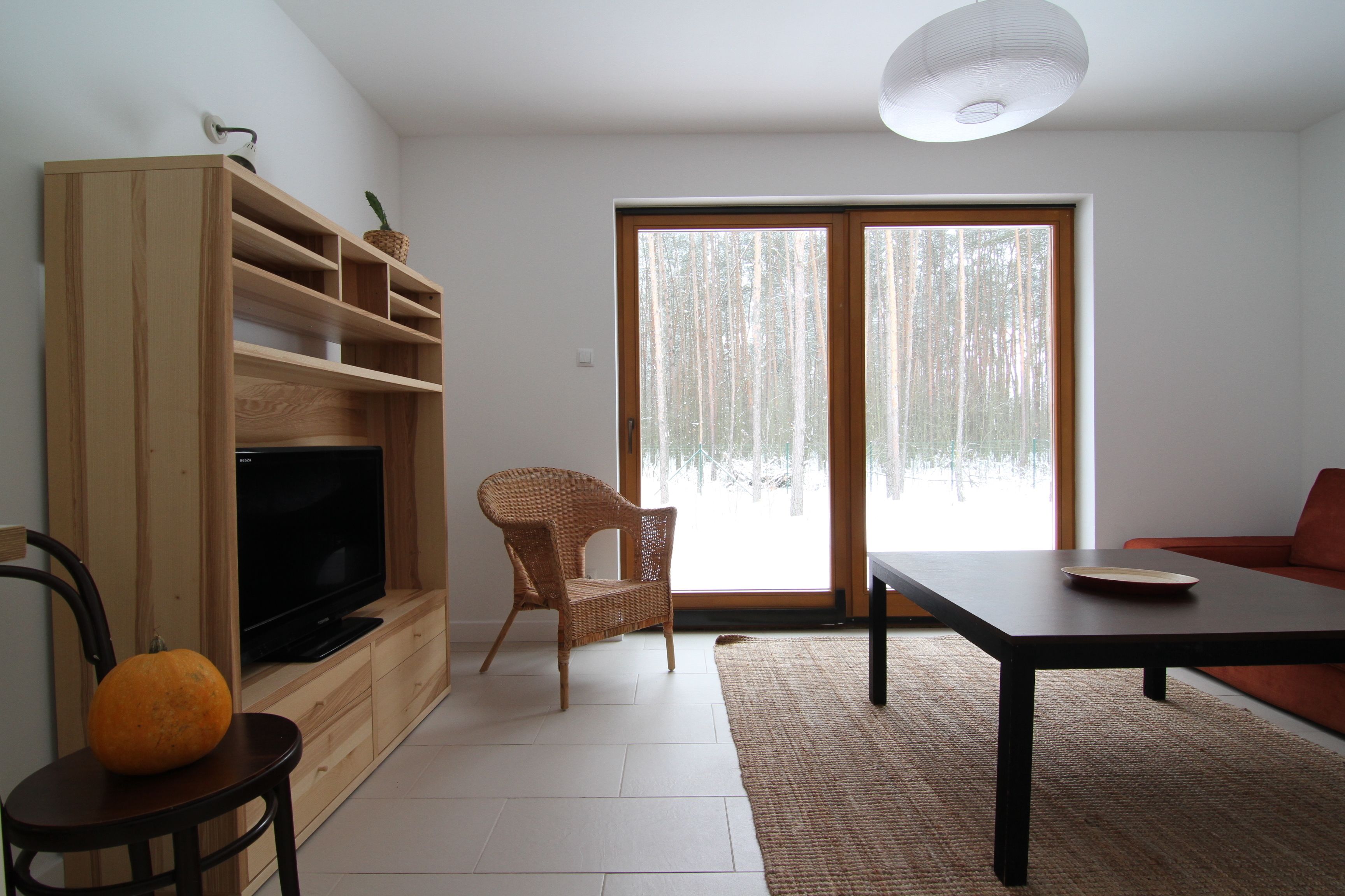 A living room with a TV, a wooden entertainment unit, a wicker chair, a dining table, and a sofa.
