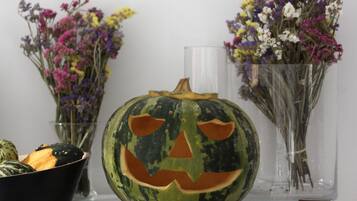 Una calabaza tallada con rostro sobre una superficie blanca, flanqueada por dos jarrones con flores.