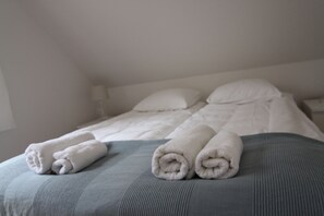 A neatly made bed with a grey bedspread and two rolled white towels on it. - Osada Osjaków (Osjakow)