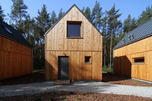 A wooden cabin with a gabled roof, a small window, and a door. - Osada Osjaków (Osjakow)