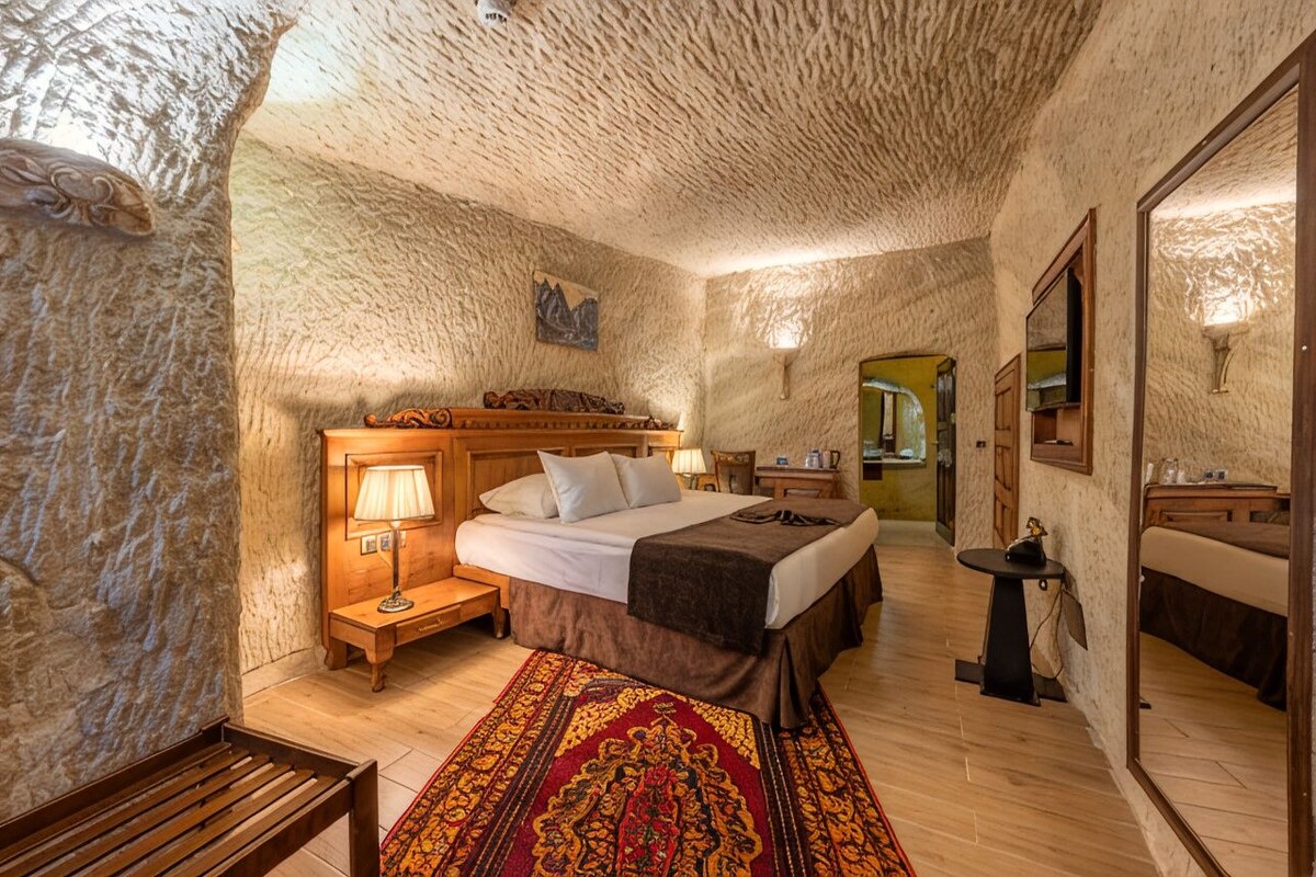 A room with a bed, bedside table, lamp, and a mirror.
