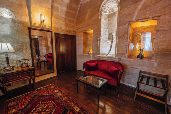 A room with a wooden floor, a red sofa, a glass coffee table, a wooden cabinet, a mirror, and a patterned rug. - Utopia Cave Cappadocia (Ürgüp)