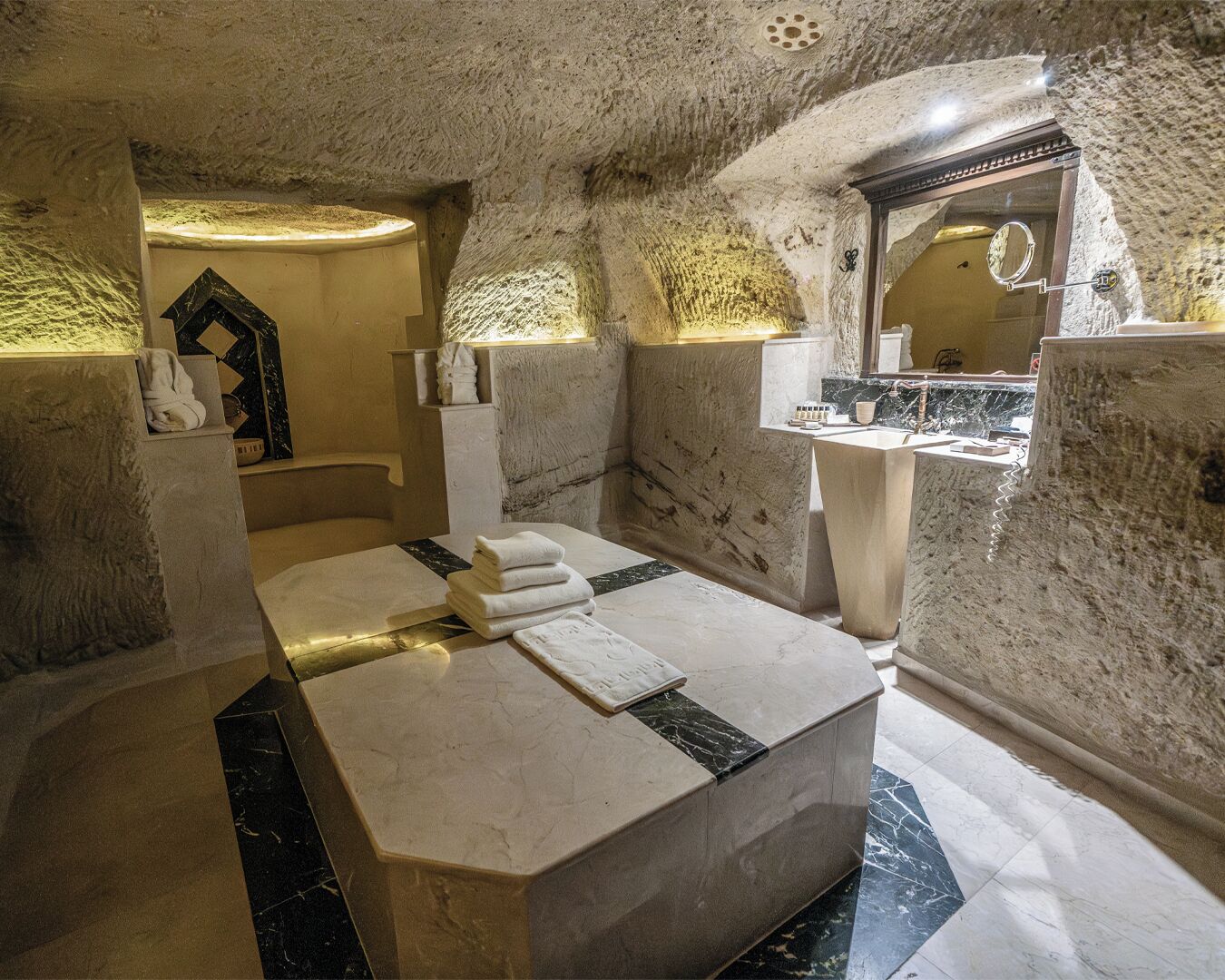 A stone-walled bedroom with a large bed, a marble-topped vanity, and a bathtub.