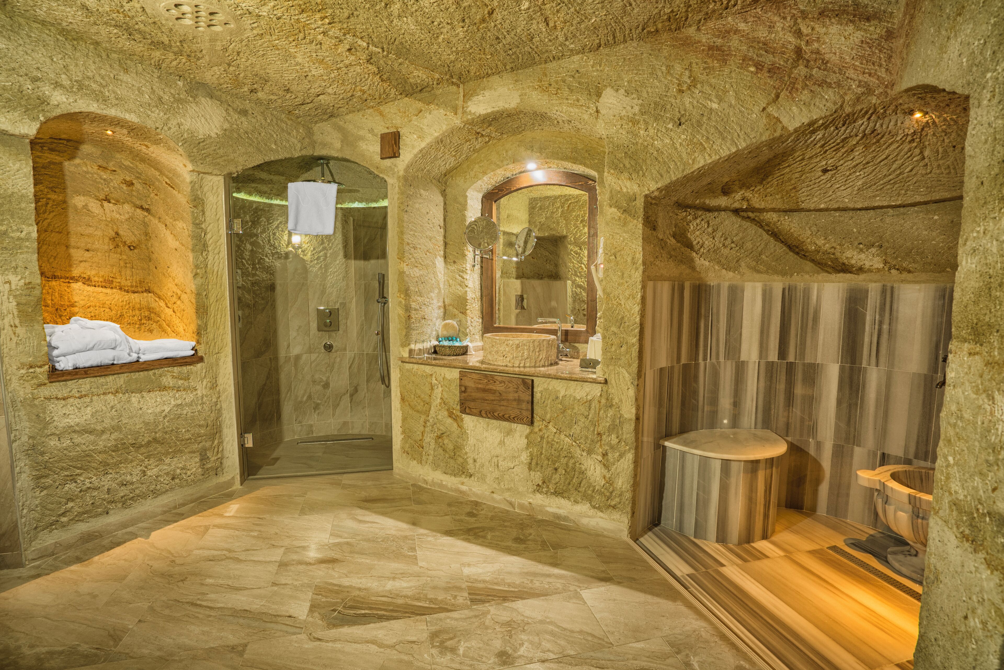 Un baño con paredes de piedra, un tocador de madera, un espejo y una bañera.