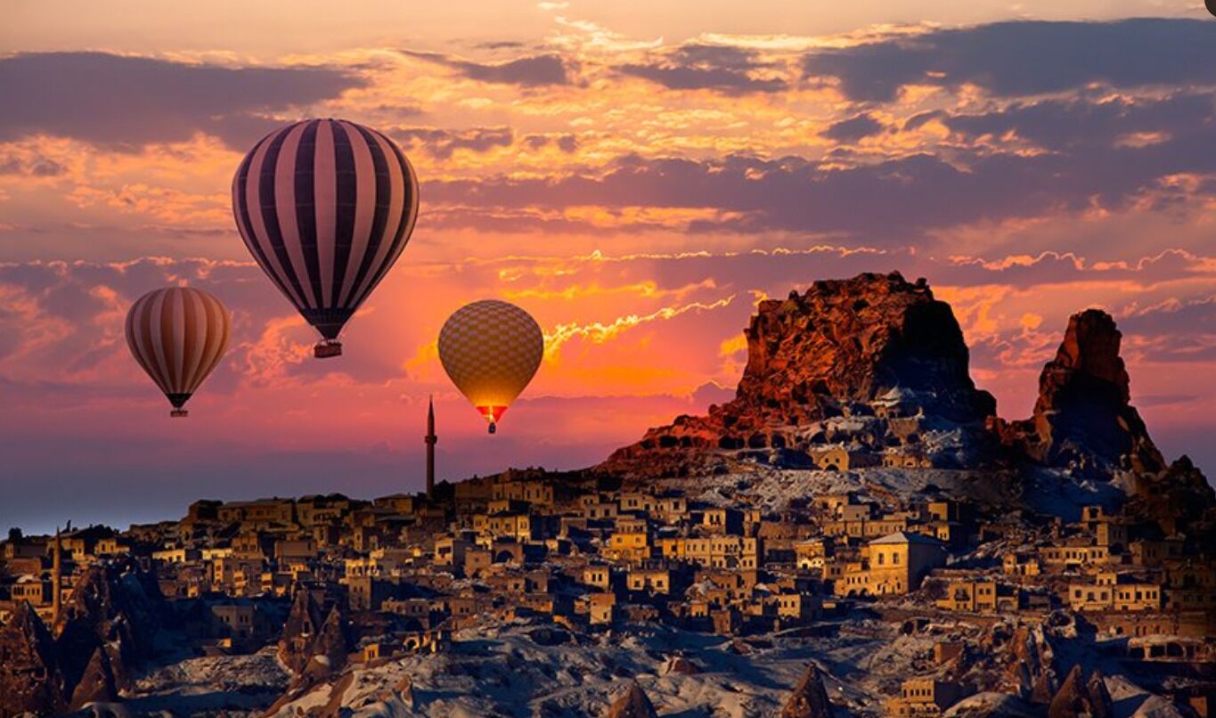 Paisaje urbano con un atardecer y globos aerostáticos.