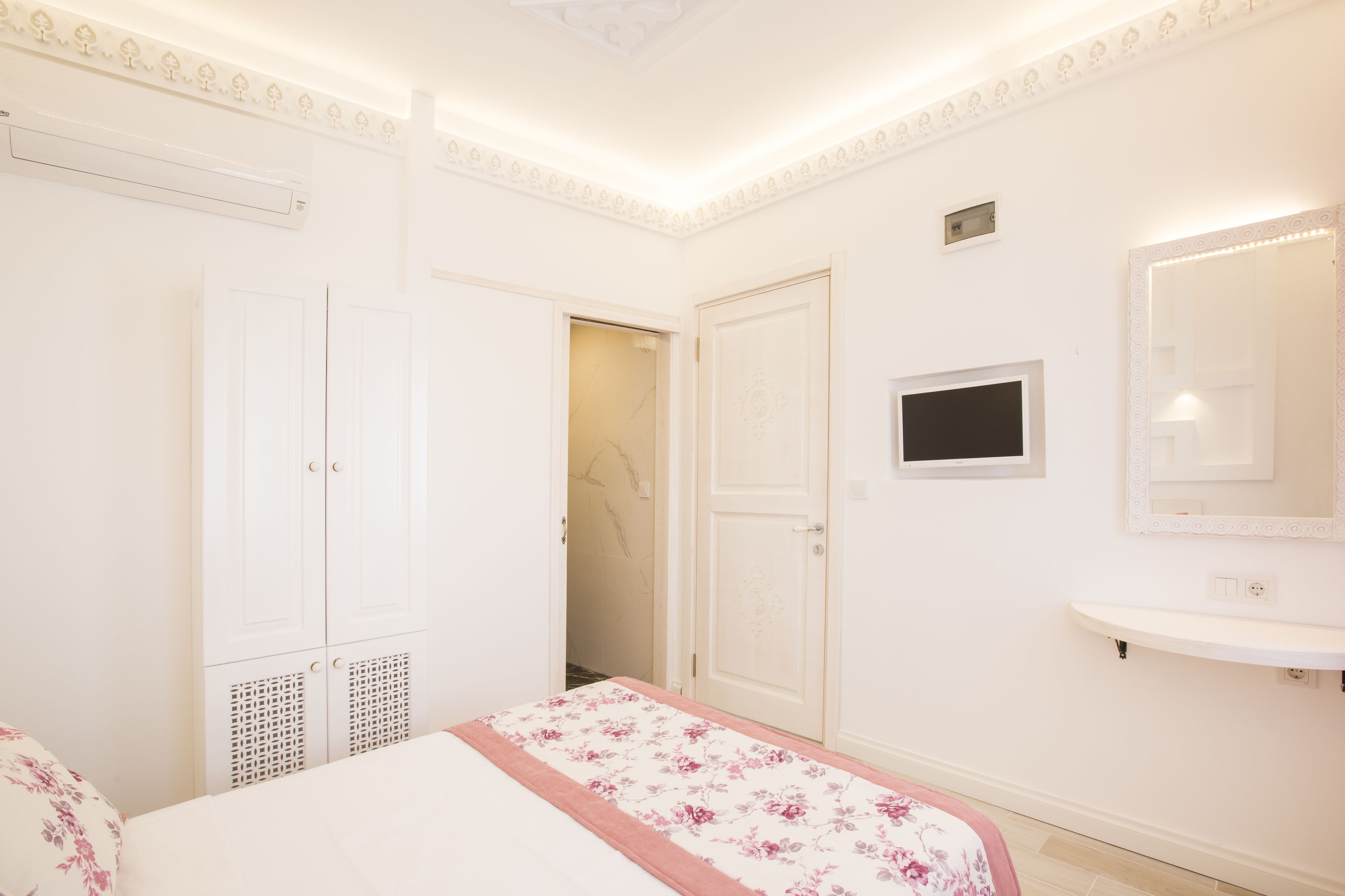 A bedroom with a bed, a wardrobe, a mirror, and a small television.