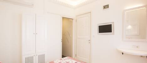 A bedroom with a bed, a wardrobe, a mirror, and a small television.