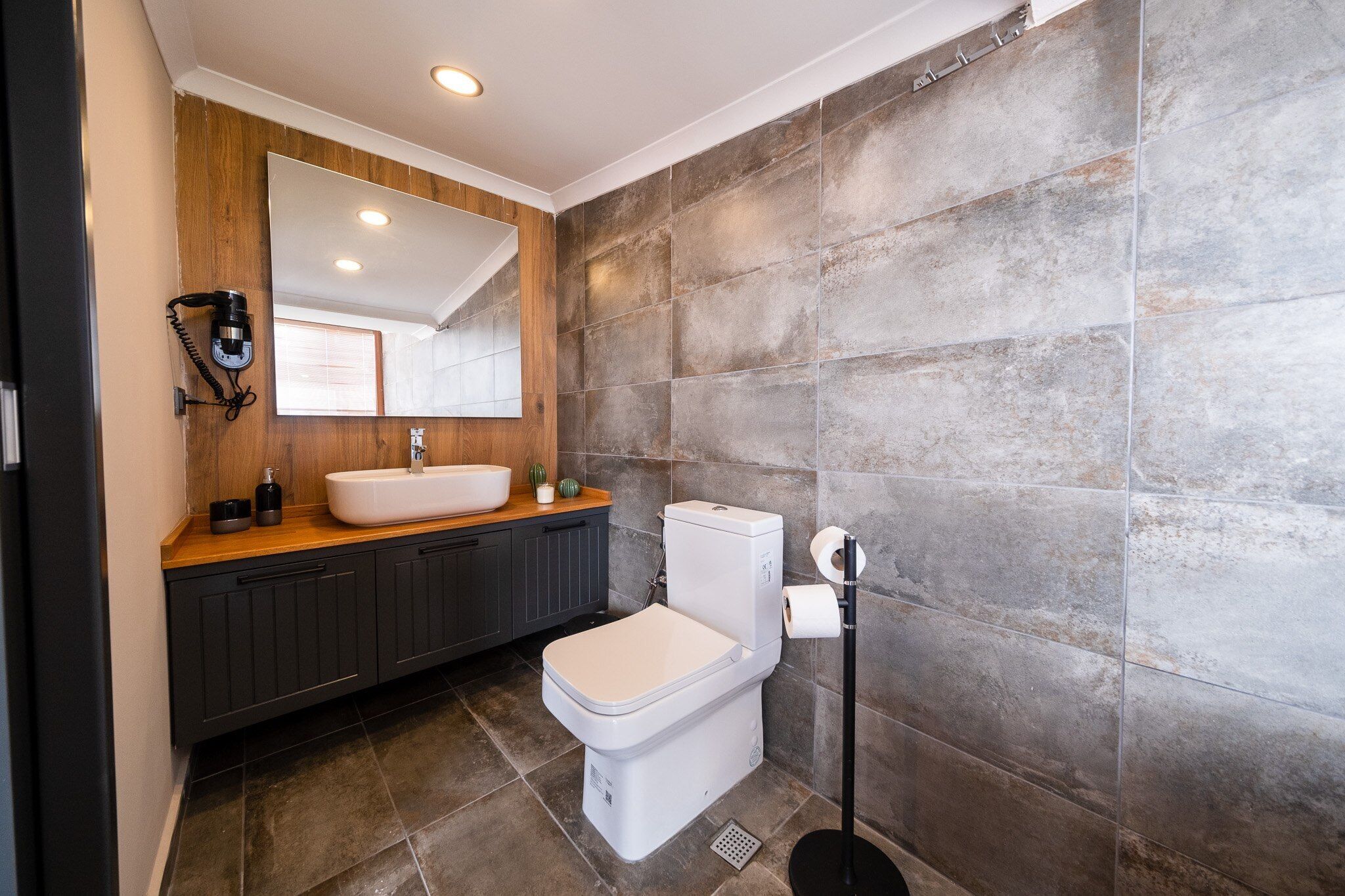 Une salle de bain moderne avec un meuble-lavabo en bois, des toilettes blanches et un grand miroir.