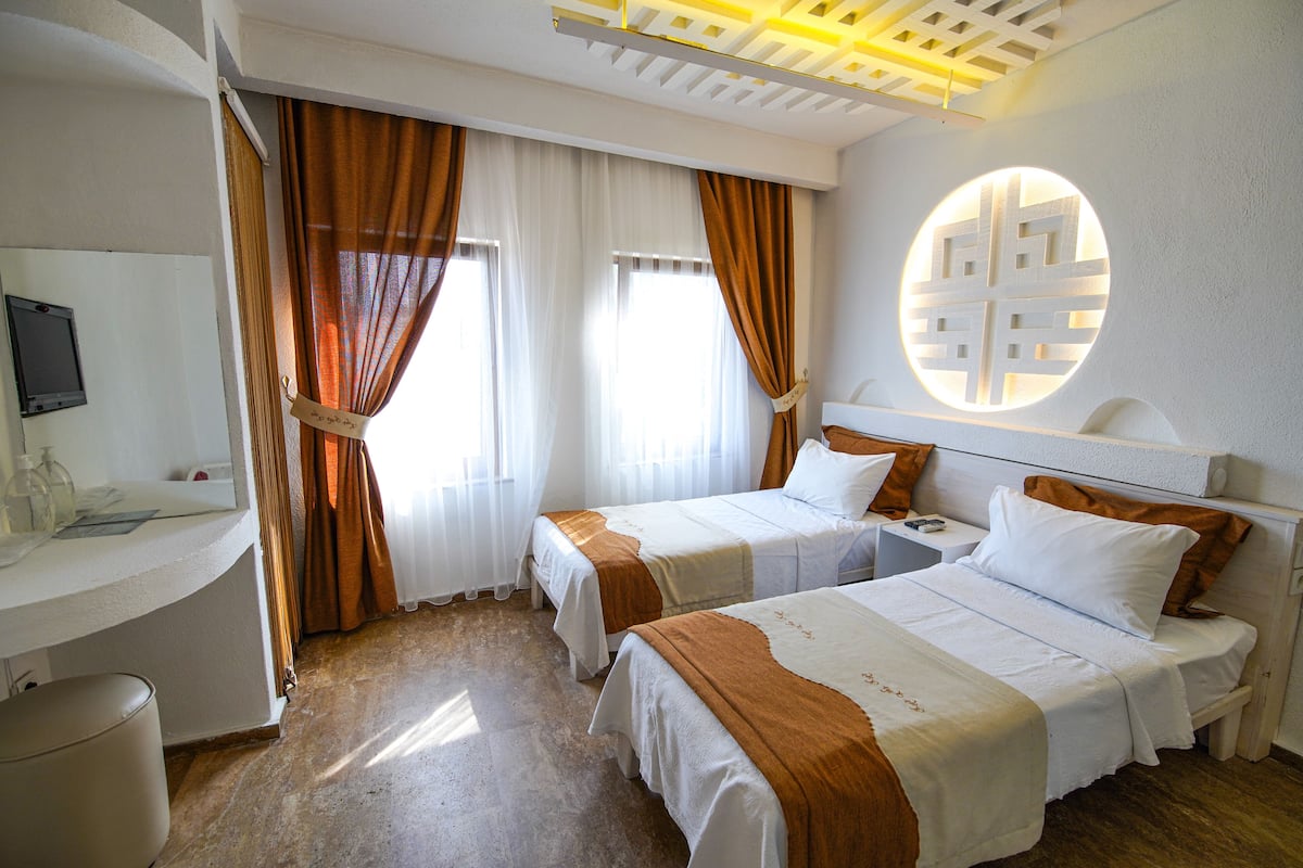 A hotel room with two beds, a desk with a chair, a TV, and a large window with curtains.
