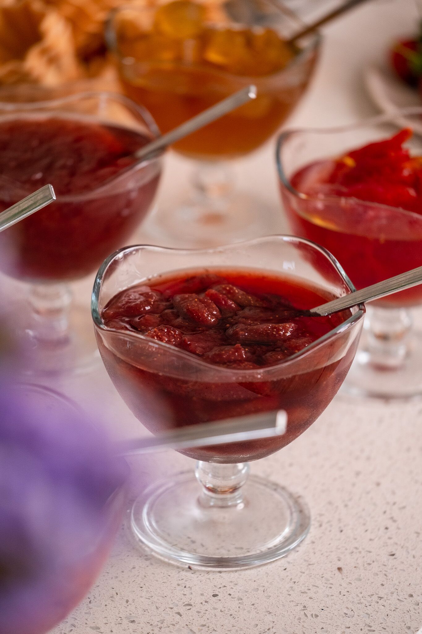 Une table dressée pour le dessert, avec plusieurs verres de vin rouge doux, un saladier de fruits et un verre de boisson à l’orange.