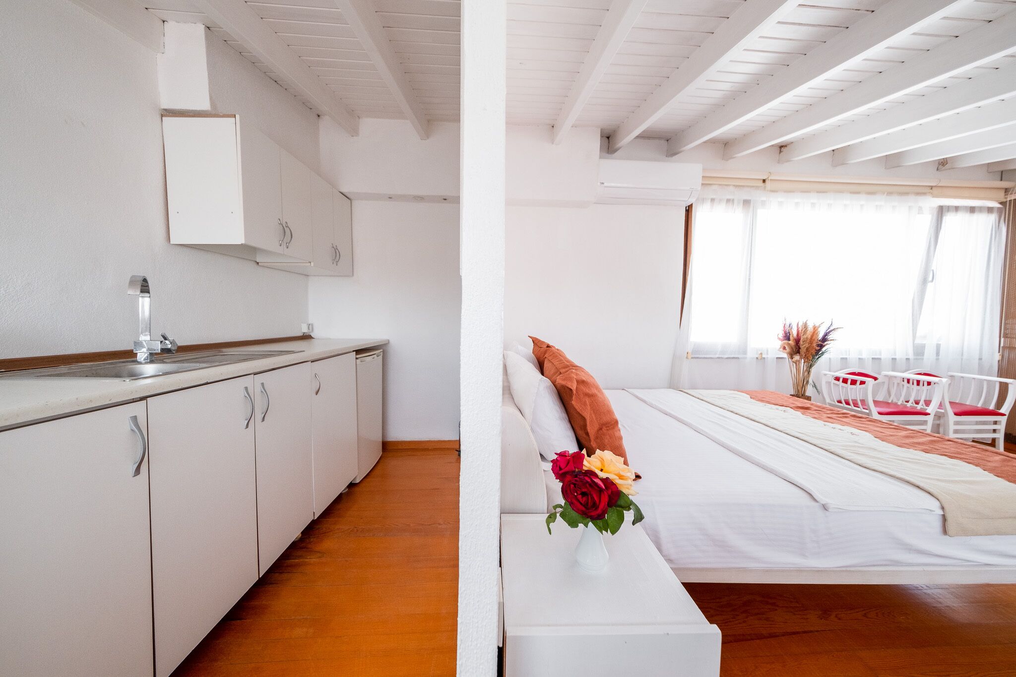 Una camera d'albergo moderna con angolo cottura, un letto con testiera bianca e vista sull'esterno tramite ampie finestre.