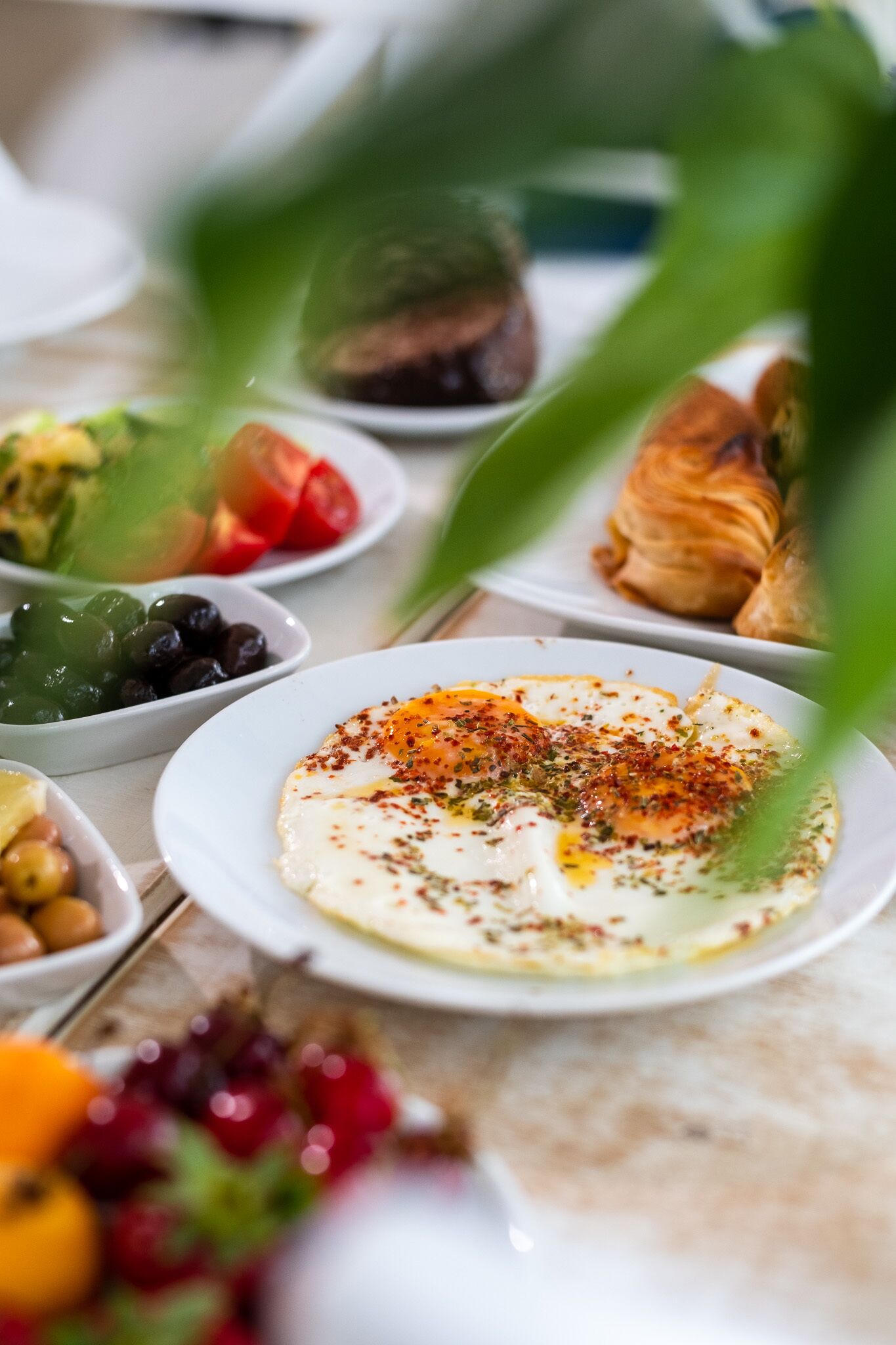 A table with various dishes including a plate of eggs, olives, and a croissant.
