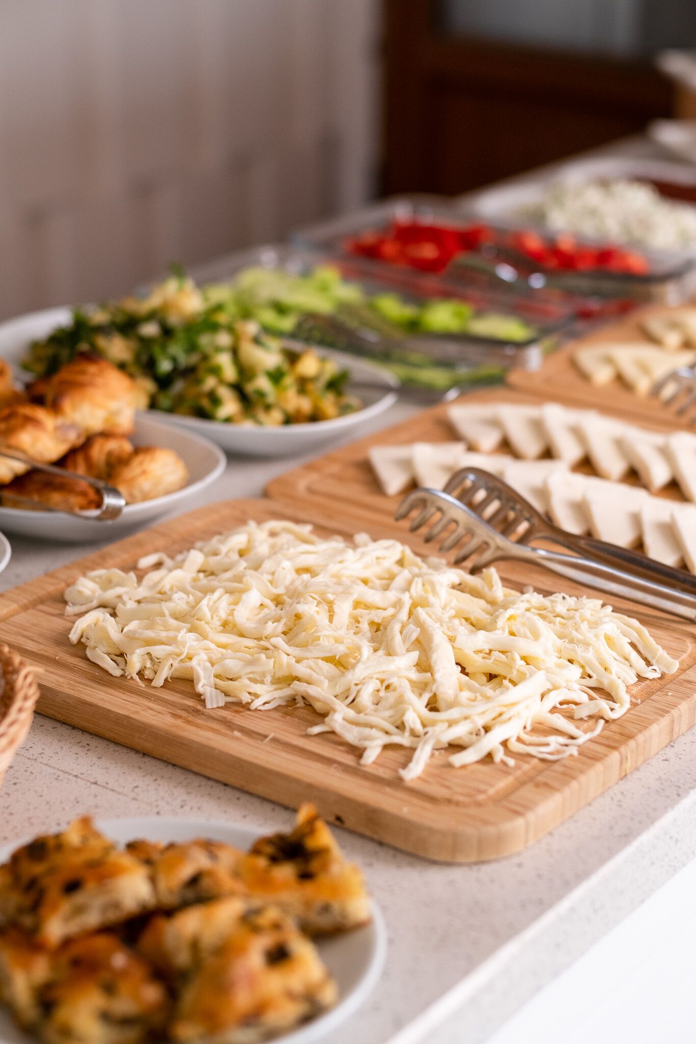 Une table de buffet proposant divers plats, notamment du fromage râpé, des croissants et une salade.