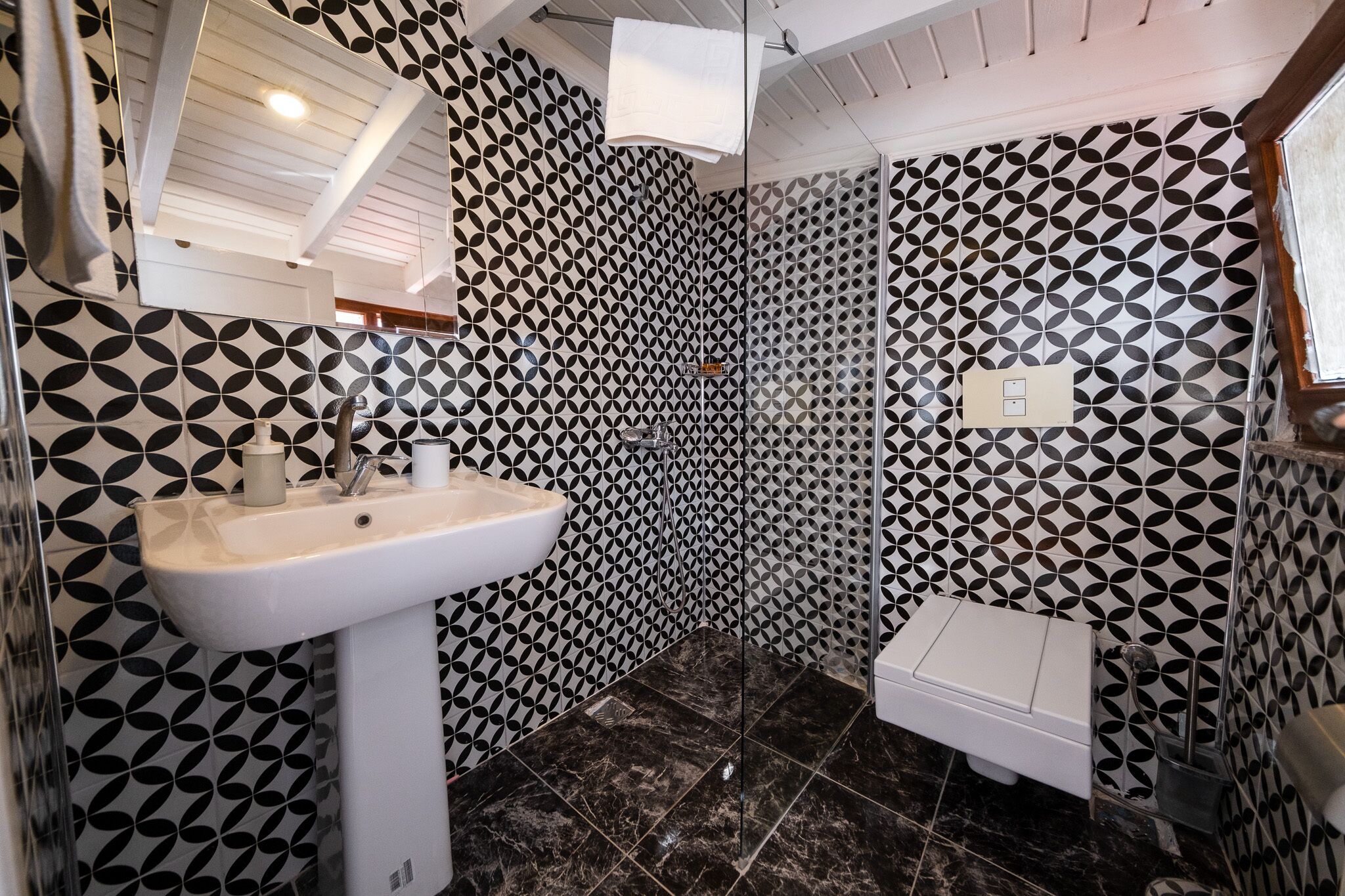 Um banheiro com parede de azulejos estampados em padrão geométrico, pia branca e área de chuveiro.