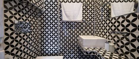 Un baño con un estampado geométrico blanco y negro, un lavamanos blanco y dos toallas blancas colgadas en la pared.
