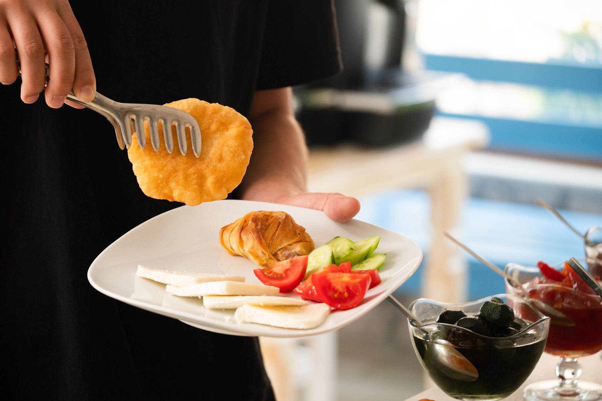 Una persona sosteniendo un plato con un croissant, tomates, pepinos y queso.