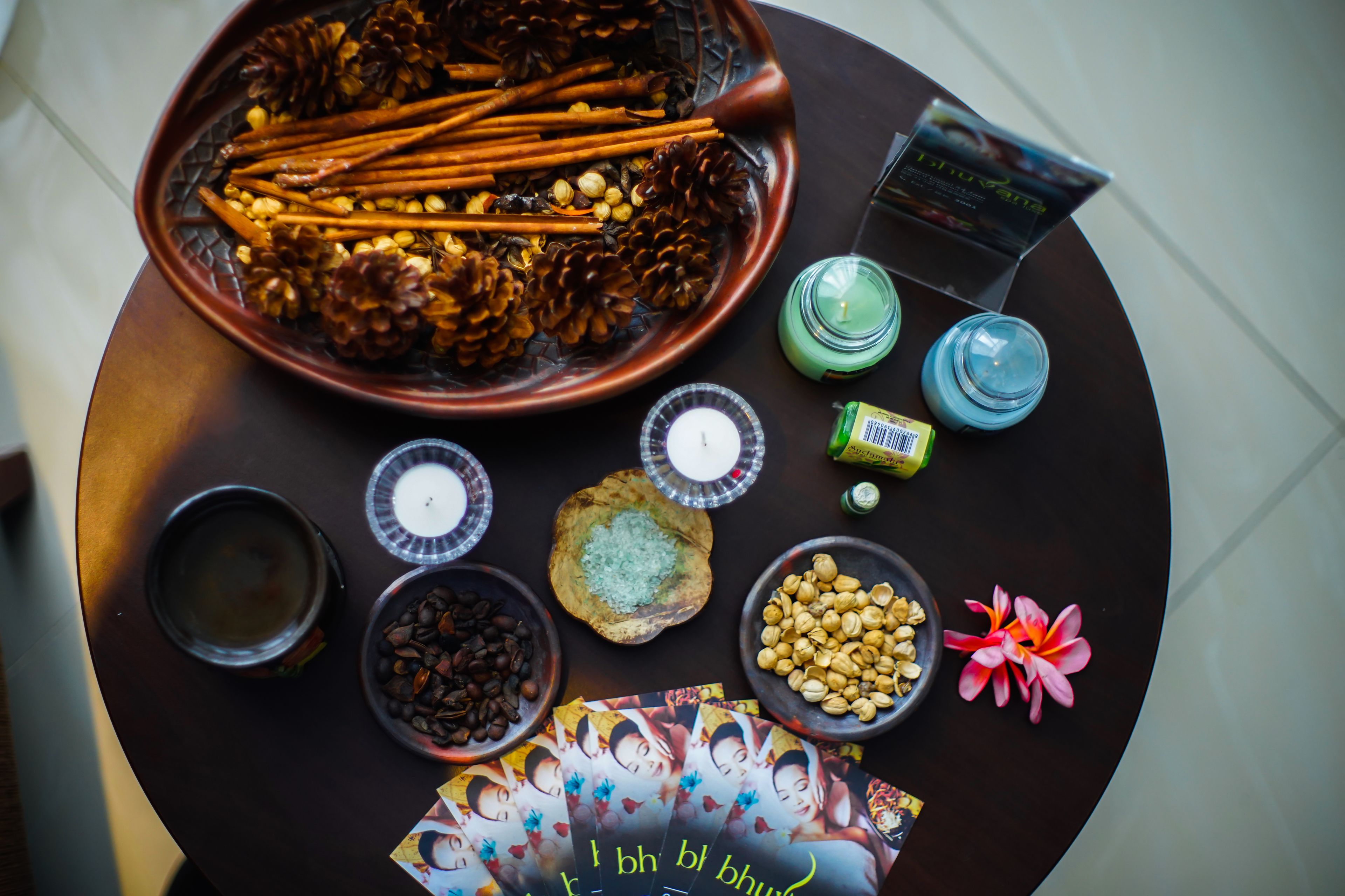 A table with various items including a bowl of pinecones, cinnamon sticks, coffee beans, a candle, and a card with text.