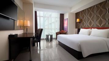 A hotel room with a bed, a desk, a chair, a TV, and a window with curtains.