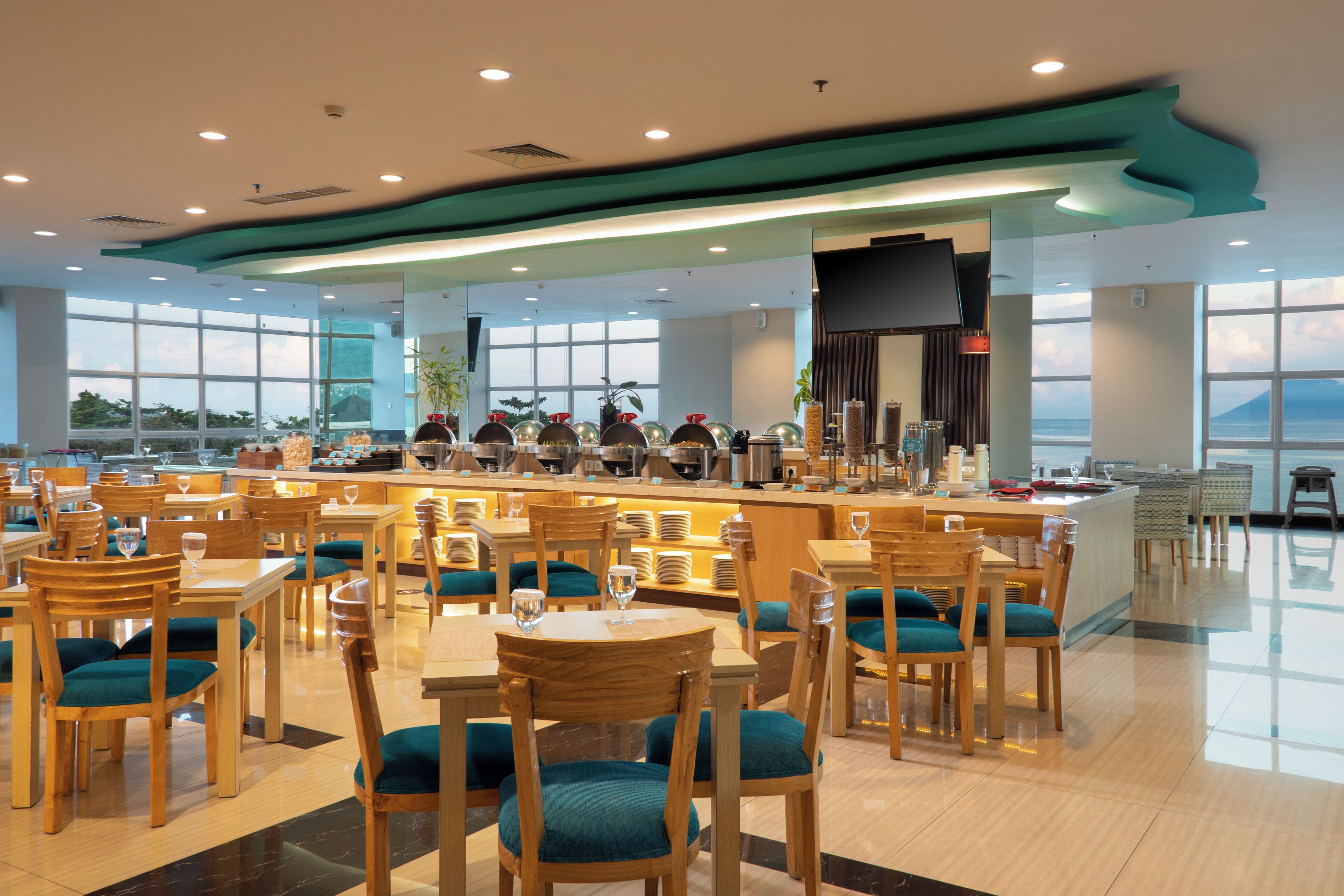 Um restaurante amplo com várias mesas e cadeiras, área de bar e grandes janelas com vista para o mar.
