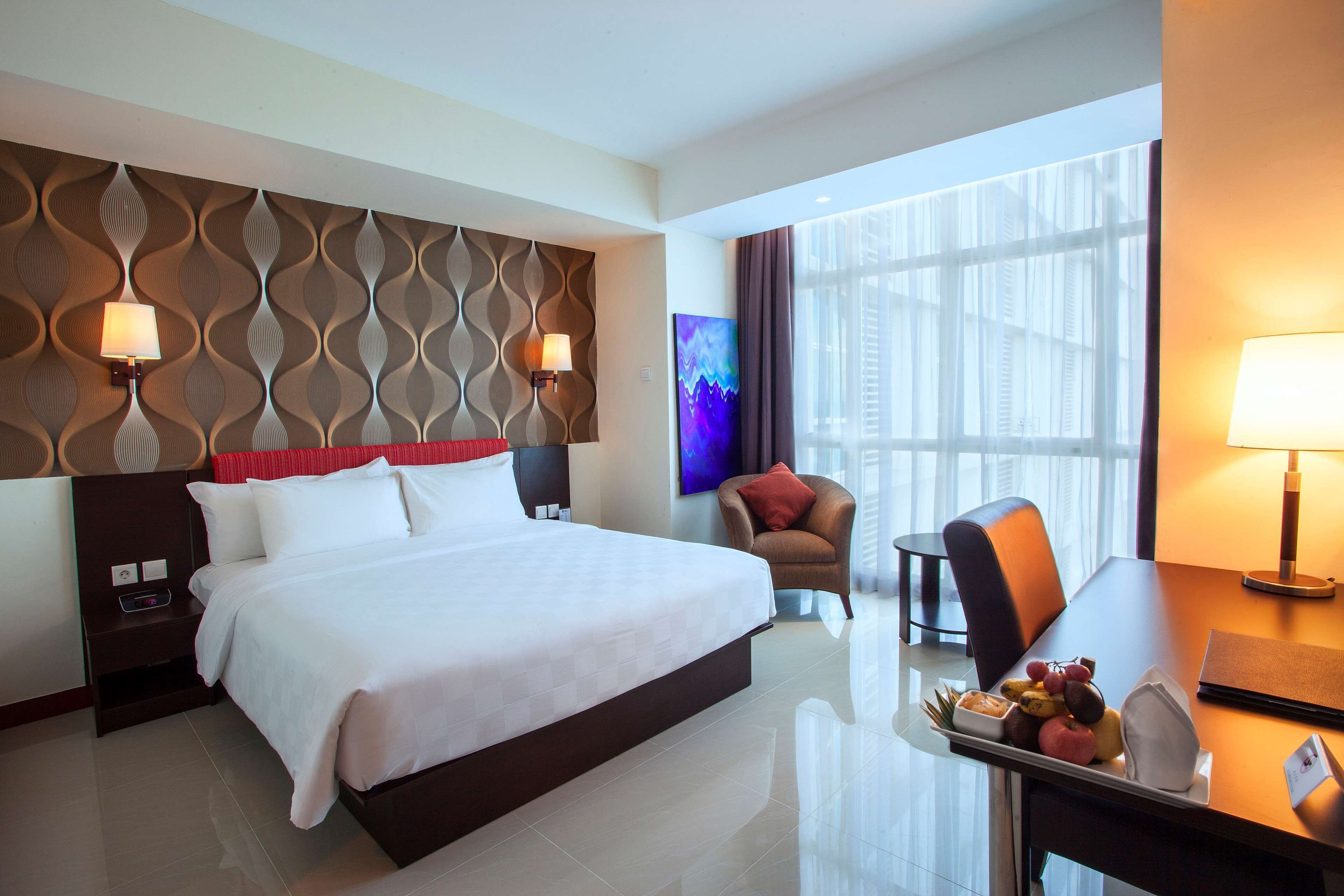 A hotel room with a large bed, a desk with a lamp, a chair, and a TV.