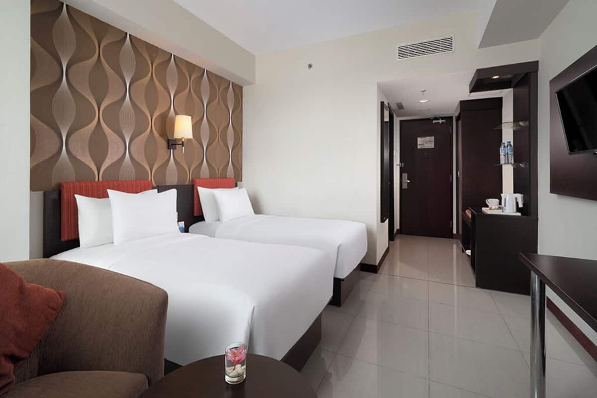 A hotel room with two beds, a TV, a desk, and a bathroom door.