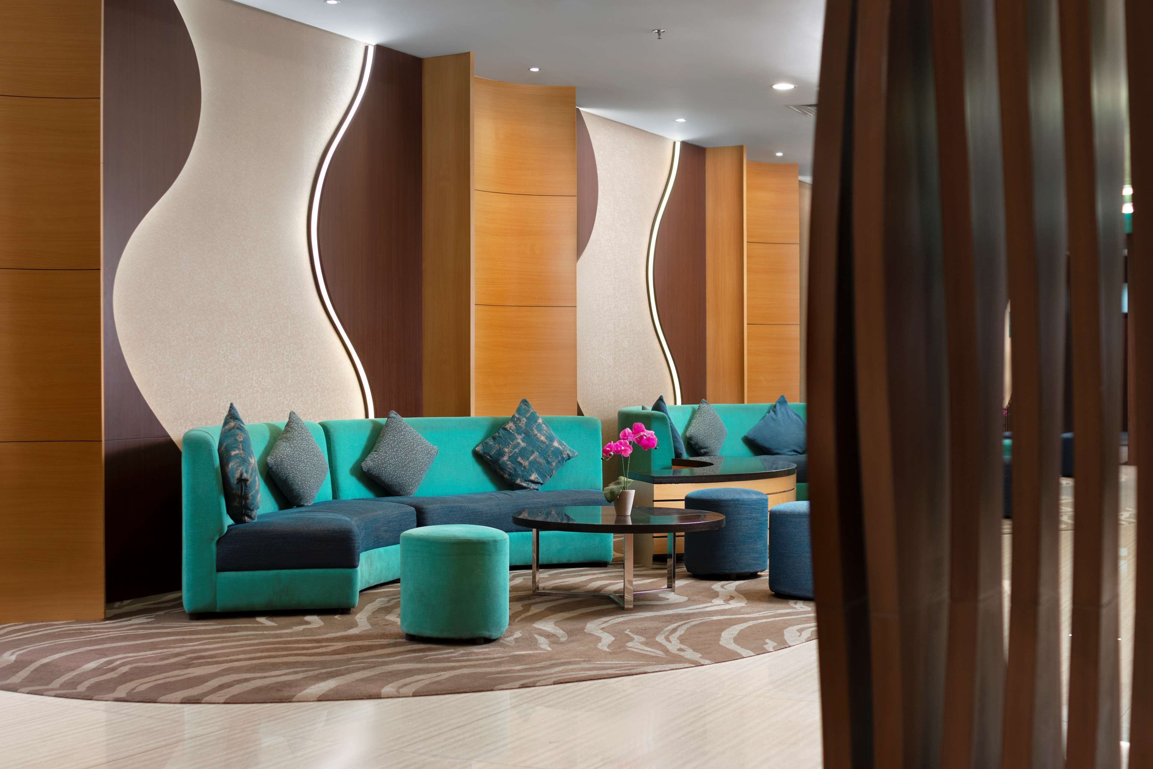 A modern lounge area with teal sofas, ottomans, and a coffee table.
