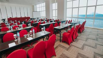 A conference room with red chairs and tables, large windows, and a view of the sea.
