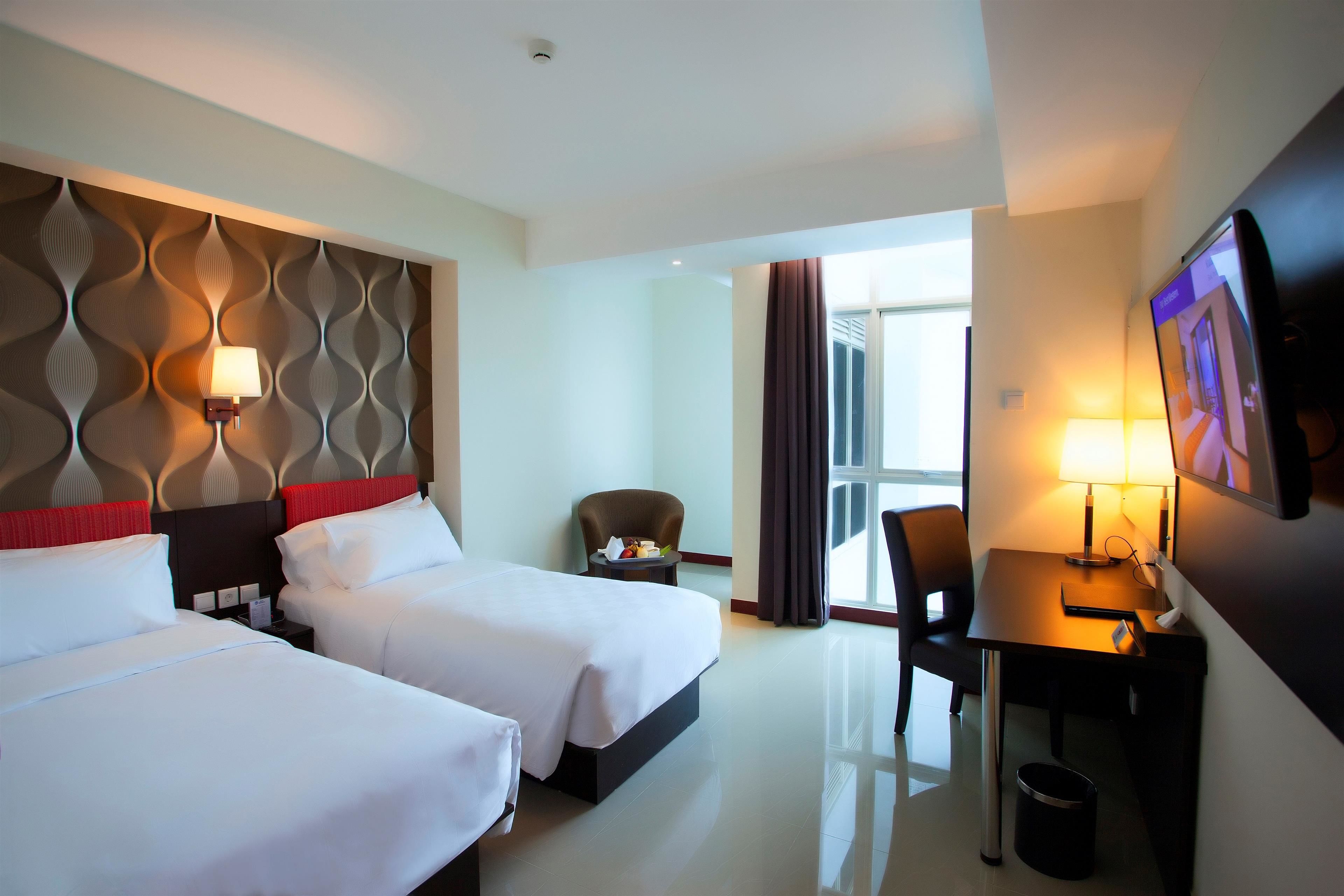A hotel room with two beds, a desk, a chair, a TV, and a window with curtains.