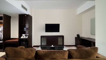 A modern living room with a brown sofa, a glass coffee table, a flat-screen TV mounted on the wall, and a dark wooden cabinet with a mirror.