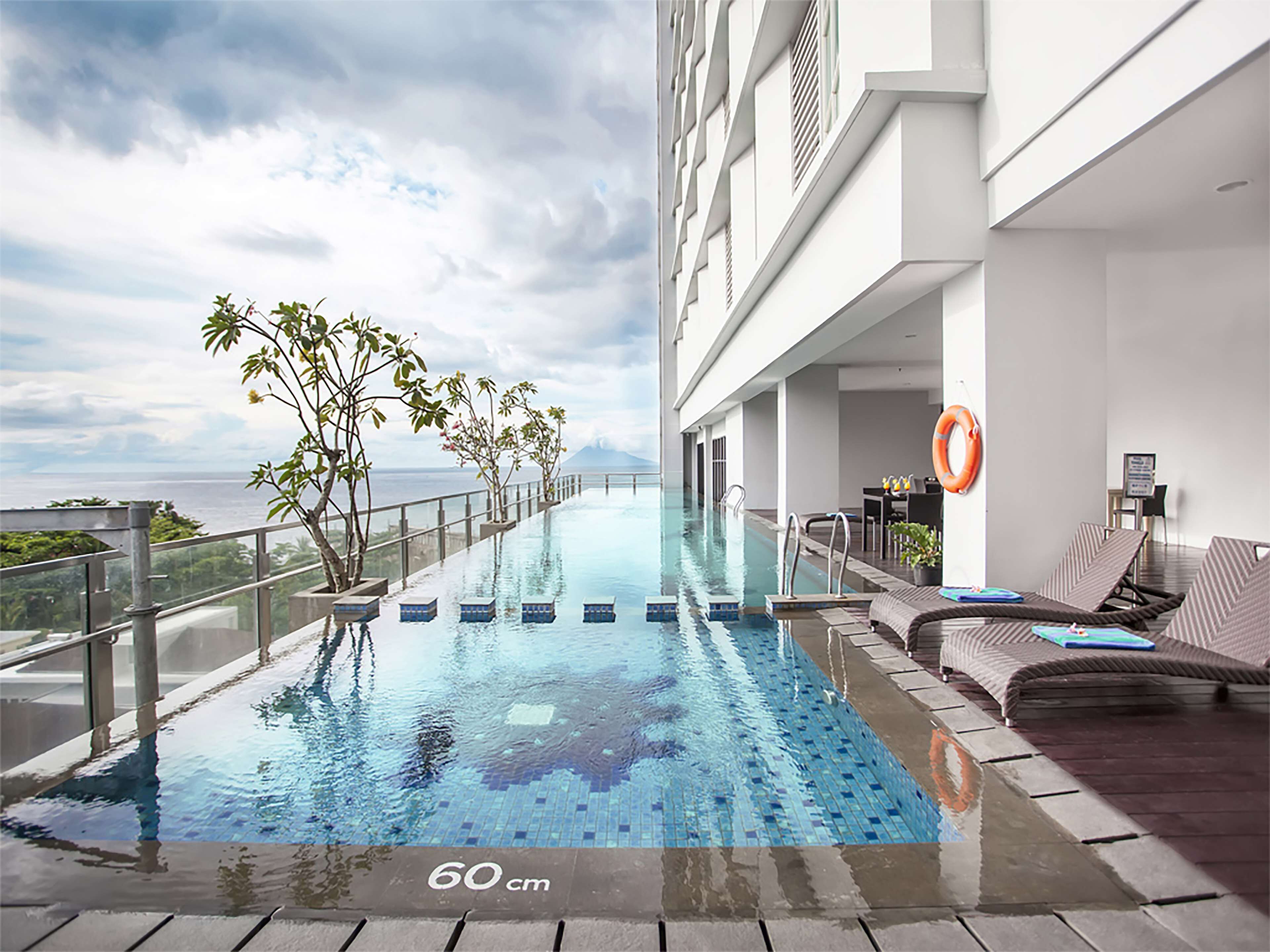 A rooftop infinity pool with a view of the ocean, surrounded by lounge chairs and potted plants.