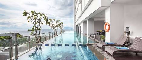 A rooftop infinity pool with a view of the ocean, surrounded by lounge chairs and potted plants.