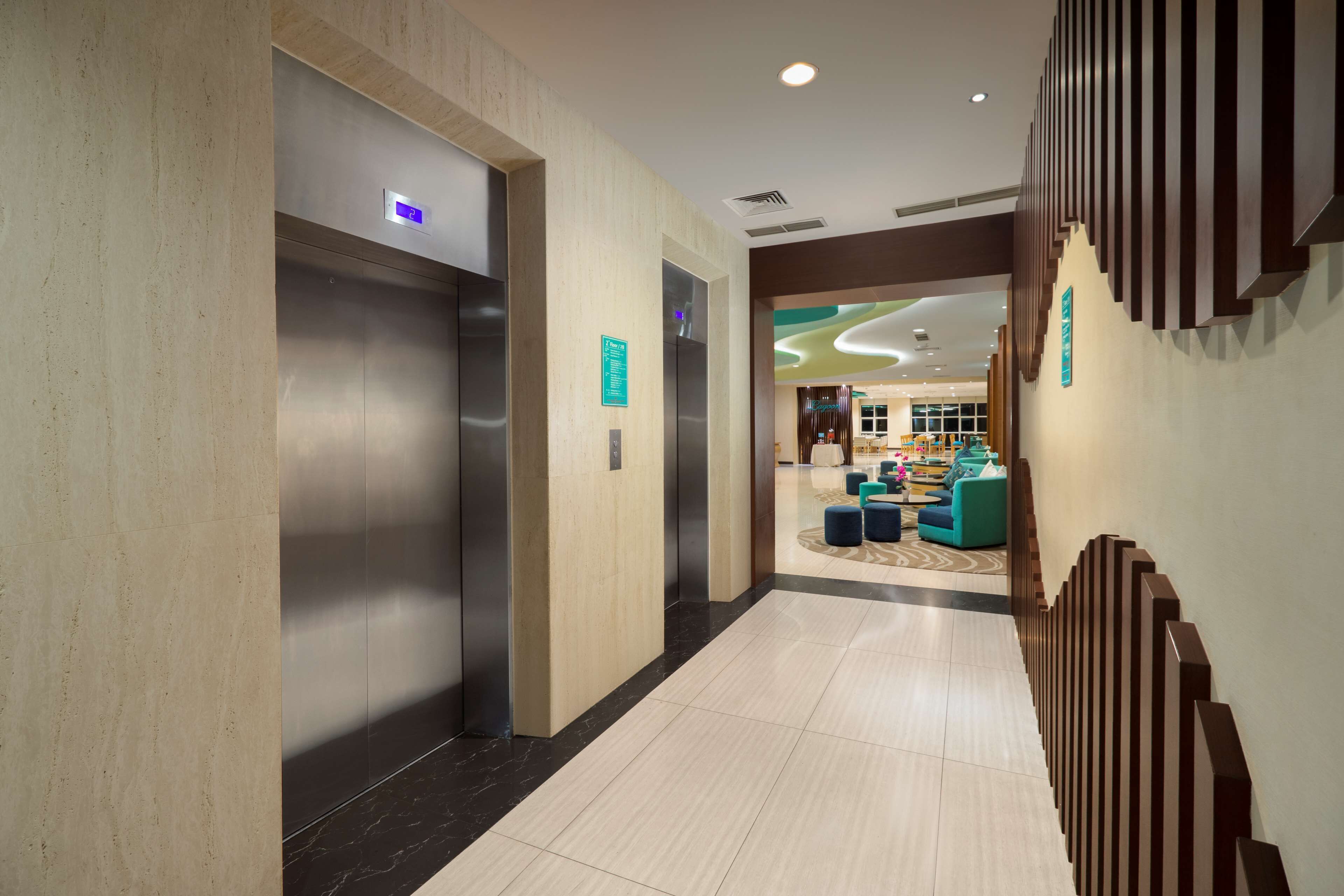 Un moderno vestíbulo de hotel con ascensores, una zona de recepción y un área de descanso con sillas coloridas.