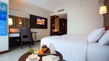 Une chambre d’hôtel équipée d’un lit, d’un bureau, d’une télévision et d’un plateau de petit-déjeuner avec des fruits et un bol.
