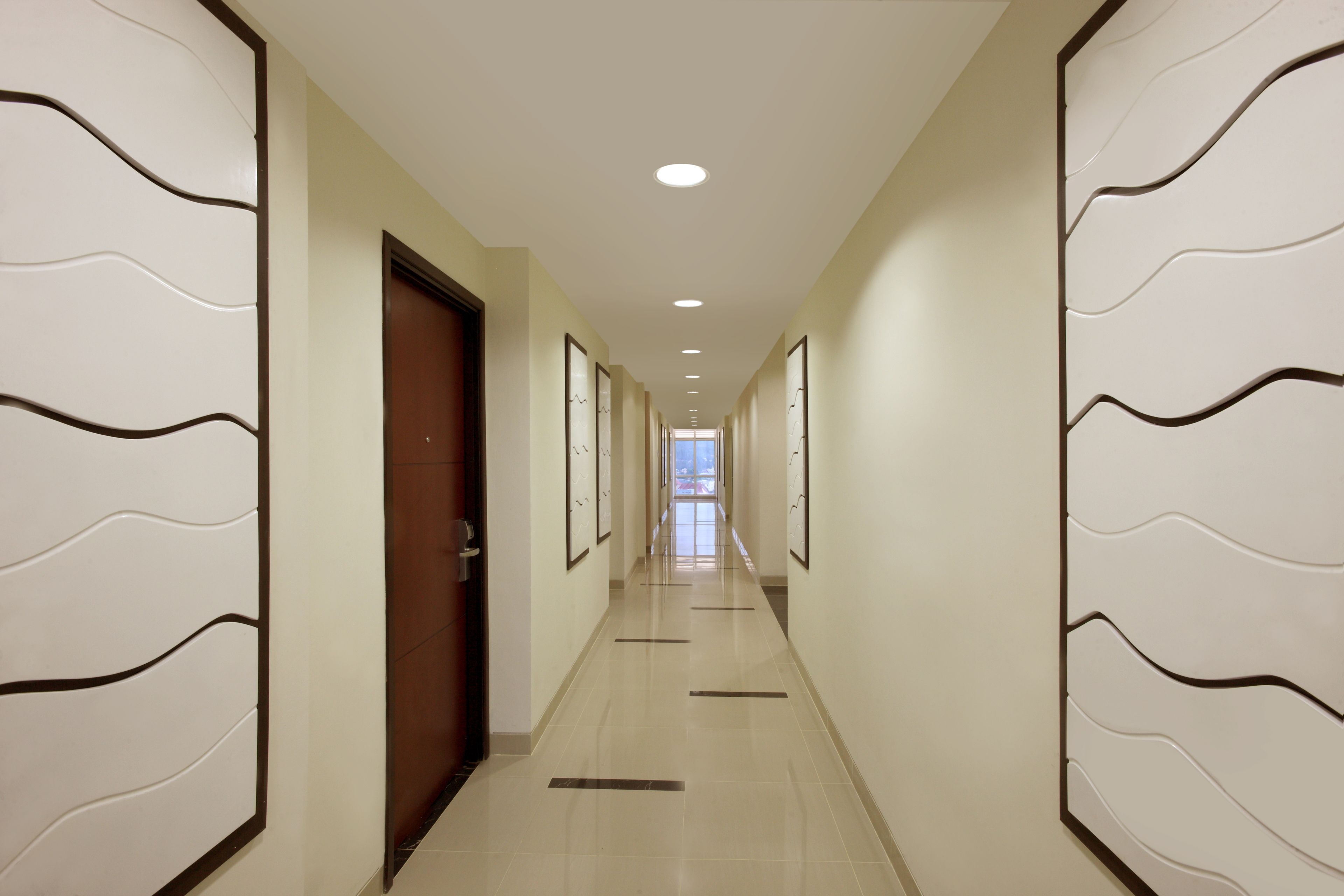 A long, narrow hallway with a wooden door on the left and a series of framed pictures on the walls.