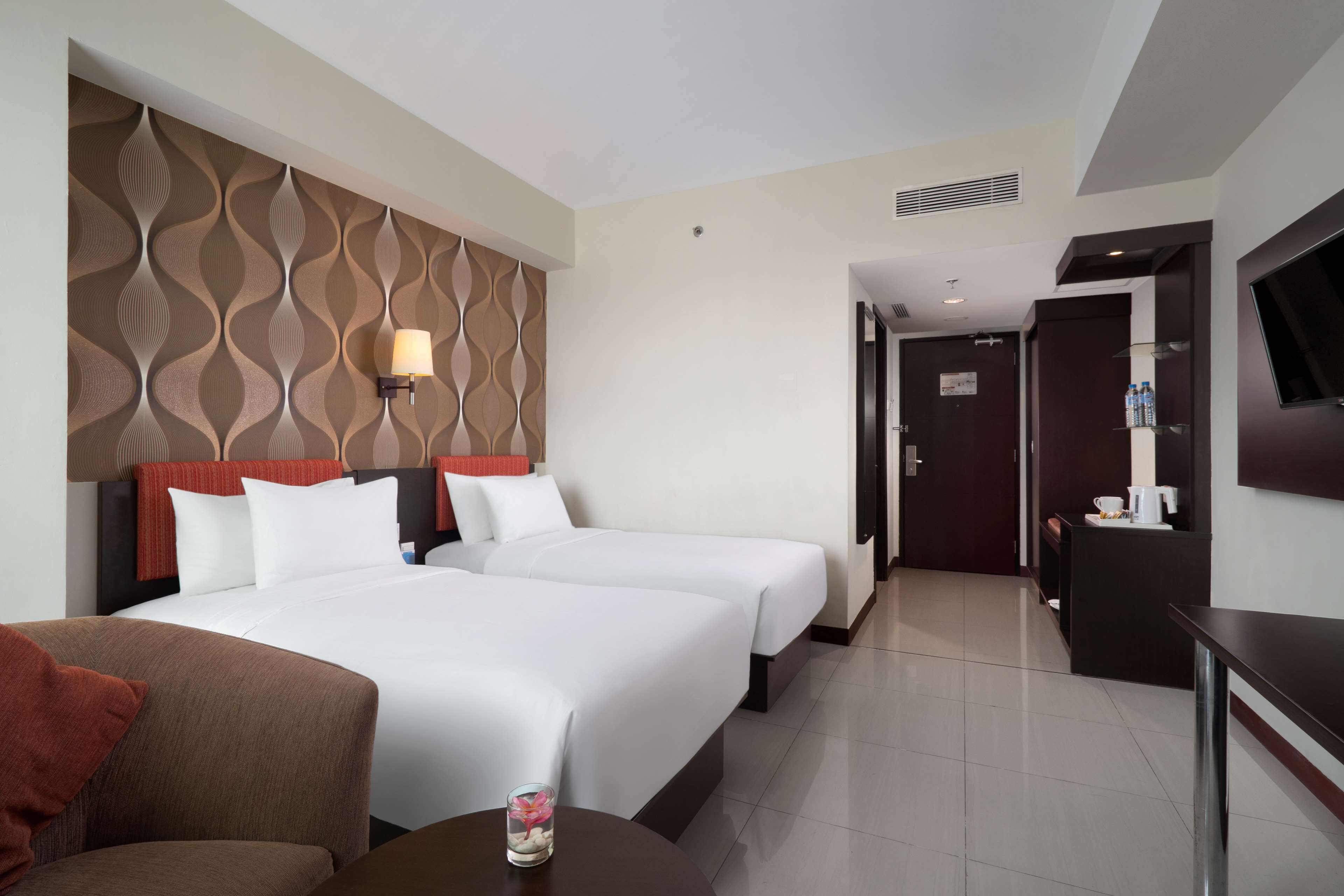 A hotel room with two beds, a TV, a desk, and a bathroom visible through an open door.
