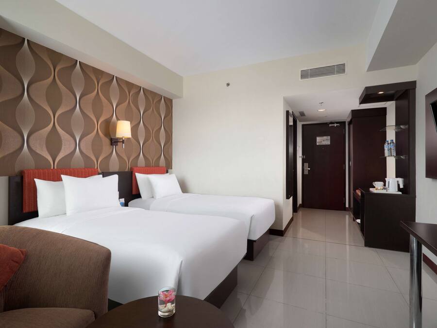 A hotel room with two beds, a TV, a desk, and a bathroom visible through an open door.