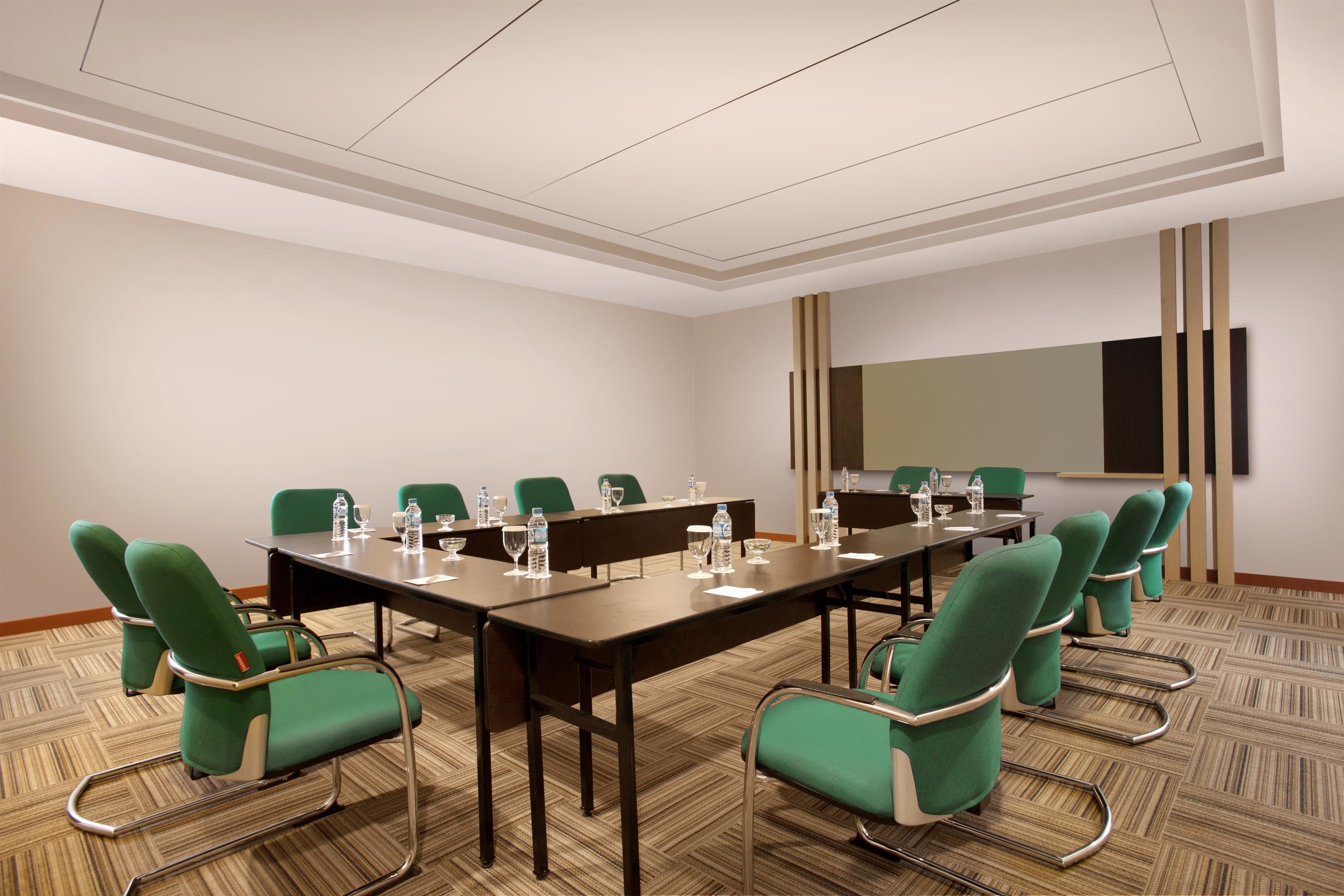 A conference room with a long table, green chairs, and a projector screen.