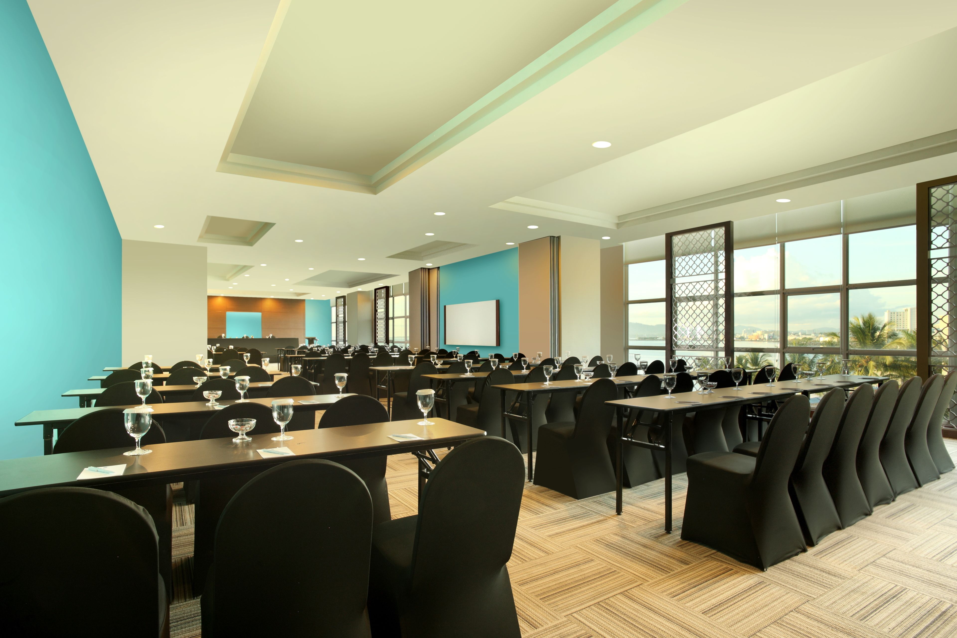 A conference room with rows of tables and chairs, large windows with a view, and a presentation screen.